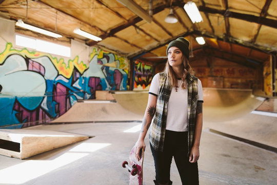 Portrait confident young female skateboarder at indoor skate park