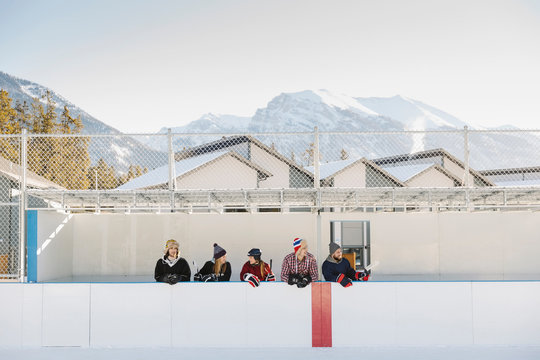 Friends standing at outdoor ice hockey sideline below mountains