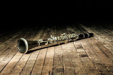 black woodwind clarinet lies on a brown wooden stage - obrazy, fototapety, plakaty