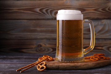 A large mug of cold, fresh, tasty, lager beer with foam and a snack of salted pretzels and sticks.