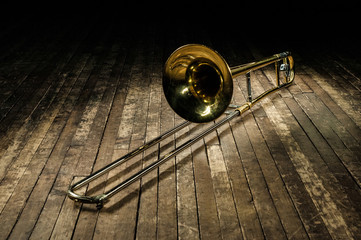 golden brass instrument trombone lies on a brown wooden stage © Chernobrovin