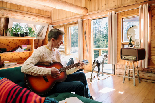 Man With Dog Playing Guitar In Cabin