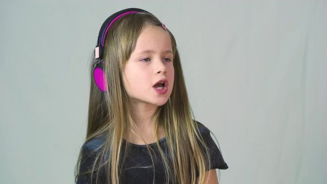 Pretty smiling cild girl listening to music in big pink earphones.