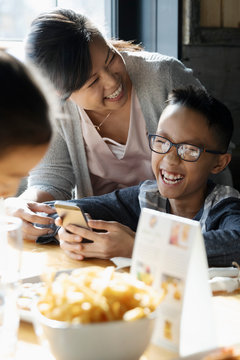 Happy, laughing family with smart phone dining at restaurant table