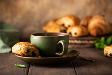 Green cup of tea with mini chocolate bun, puff pastry on old wooden table. Tasty tea break concept, copy space.