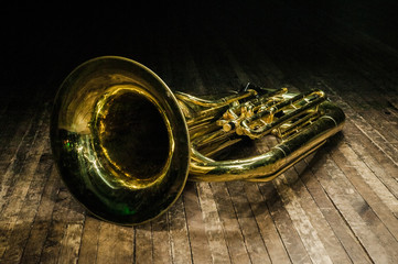 golden brass instrument tuba lies on a brown wooden stage in the light of the spotlight. - obrazy, fototapety, plakaty