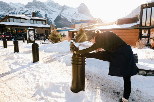 Teenage girl runner stretching leg on post in snowy mountain town