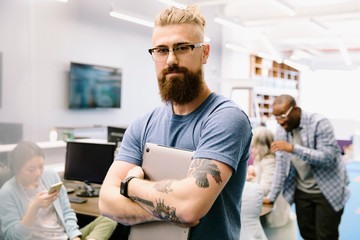 Portrait confident creative businessman with tattoos holding laptop in office
