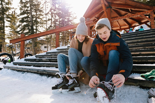 Young Couple Tying Ice Skates On Snowy Steps