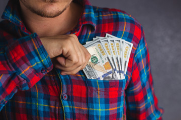 Close up hand of a man in a red and blue plaid shirt holding banknote into pocket. Man pulls money out of his breast pocket. 100 US Dollar banknote