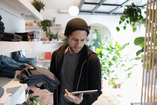 Male Business Owner With Digital Tablet Arranging Display In Menswear Clothing Shop