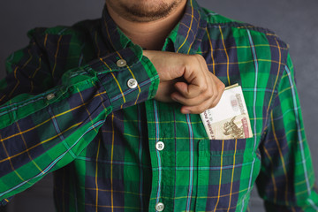 Close up hand of a man in a green plaid shirt holding banknote into pocket. Man pulls money out of his breast pocket. 100 Russian Ruble currency