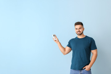 Young man with air conditioner remote control on color background