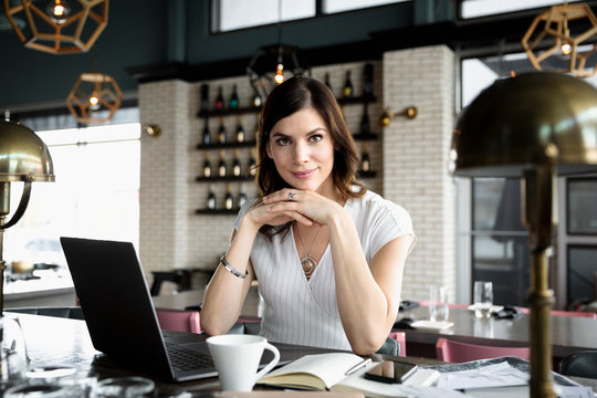 Portrait confident businesswoman working at laptop in wine bar