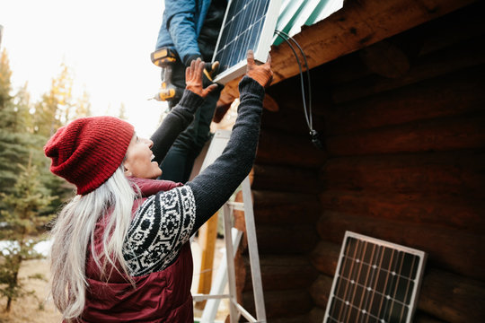 Happy woman installing solar panels on cabin