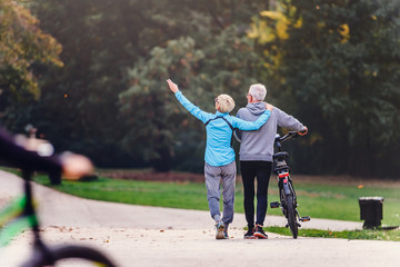 Cheerful active senior couple with bicycle walking through park together. Perfect activities for...