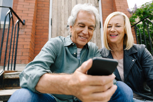 Senior couple using smart phone on front stoop