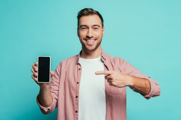 smiling man pointing at smartphone with blank screen, isolated on blue