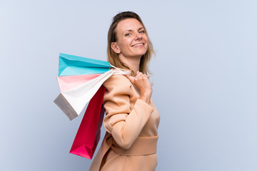 Blonde woman over isolated blue background holding shopping bags and smiling