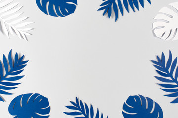 Fototapeta na wymiar Tropical paper leaves on gray background. Color of the year 2020 - Classic Blue. Color trend palette. Top view, flat lay. 