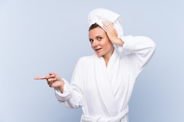 Woman in bathrobe over isolated blue background surprised and pointing finger to the side