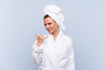 Woman in bathrobe over isolated blue background making phone gesture