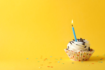 Cupcake with candle on yellow background, space for text