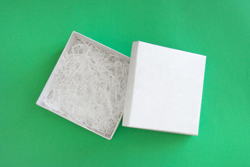 open box with cover with filling material inside lying on green colored paper background, top view