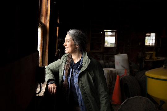 Smiling, confident female farmer looking out barn window
