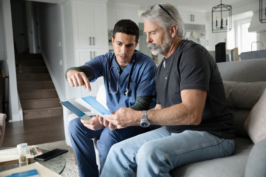 Home healthcare nurse with pamphlet talking with senior man in living room
