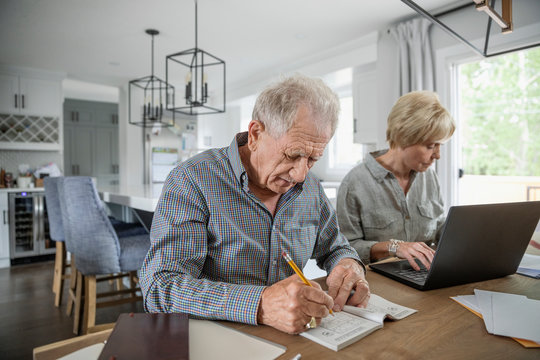 Senior couple playing sudoku and using laptop at dining table