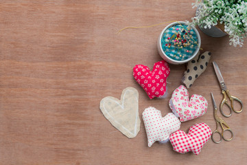 Flat lay Crafts made with fabric is a heart shape with sewing tools and accessories on a wooden background.