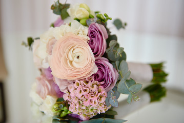 Close up of bridal bouquet of pink, violet and white roses and ranunculus with satin ribbon on mirror table, copy space. Wedding details