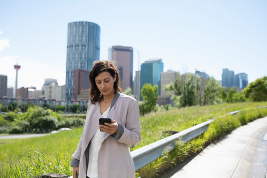 Businesswoman With Smart Phone In Sunny, Urban Park