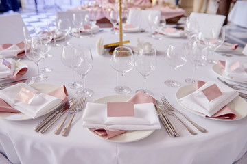 Table set with blank guest card, plate with pink and white serviette and cutlery on table, copy space. Place setting at wedding reception. Table served for wedding banquet in restaurant