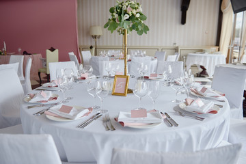 Table set with blank guest card, plate with pink and white serviette and cutlery on table, copy space. Place setting at wedding reception. Table served for wedding banquet in restaurant