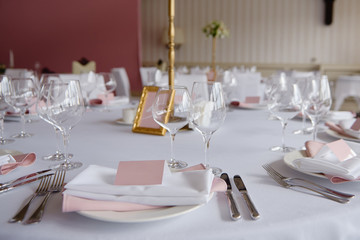 Table set with blank guest card, plate with pink and white serviette and cutlery on table, copy space. Place setting at wedding reception. Table served for wedding banquet in restaurant