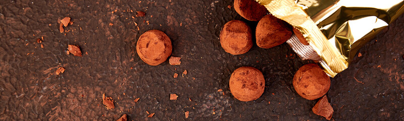 Banner with Chocolate Candy truffles fall out golden luxury box on brown background.
