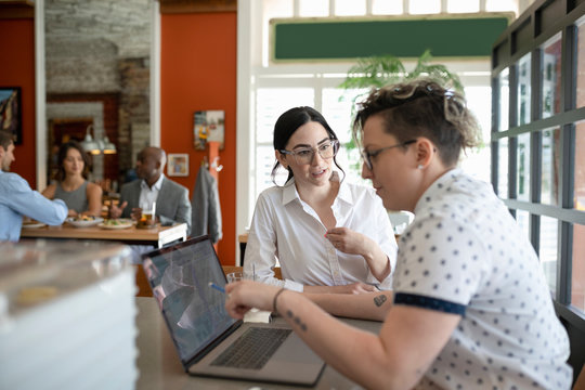 Business Owner Using Laptop Talking To Staff In Restaurant