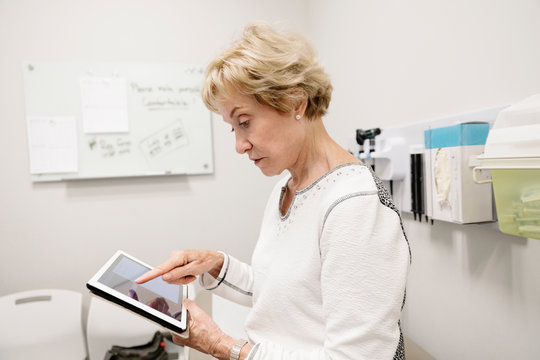 Senior female patient with digital tablet waiting in clinic examination room