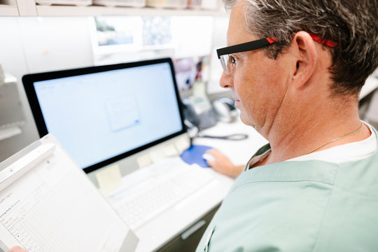 Male doctor with medical record using computer in clinic