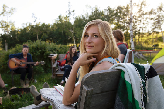 Portrait Of Young Woman Sitting In Camp With Friends Smiling At Camera