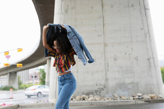 Young Woman Holding Denim Jacket Overhead In Rain