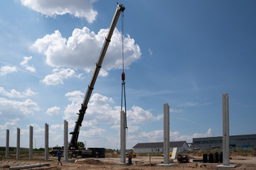 on a construction site, concrete columns for a factory building are placed with the help of a large...