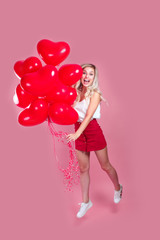 Beauty girl with red hearts air balloons laughing on pink background, Valentine's Day