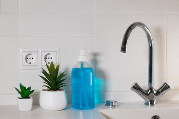 Fototapeta na wymiar Fragment of the interior of the kitchen. Liquid blue soap in a transparent plastic dispenser is located next to the sink.