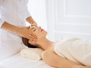 Obraz na płótnie Canvas Beautiful woman enjoying facial massage with closed eyes in spa center. Relaxing treatment concept in medicine
