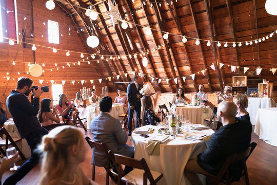 Wedding guests watching mature bride and groom kissing at wedding reception in barn