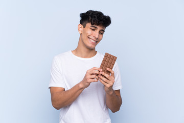 Young Argentinian man over isolated blue background taking a chocolate tablet and happy
