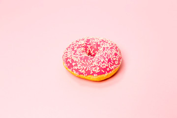 A donut in a pink glaze with a white sprinkles on a pink background. Sweets and desserts. Minimalistic background with clean place for the inscription. Copy space.
